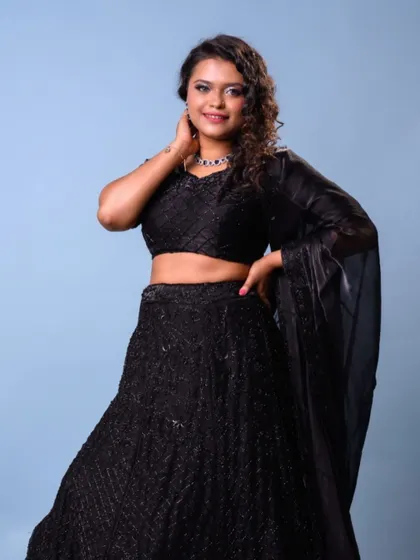 A full-length view of this gorgeous bridesmaid in a black lehenga. The makeup features a silver smokey eye and the hair is styled in tight, defined curls for a modern party look.