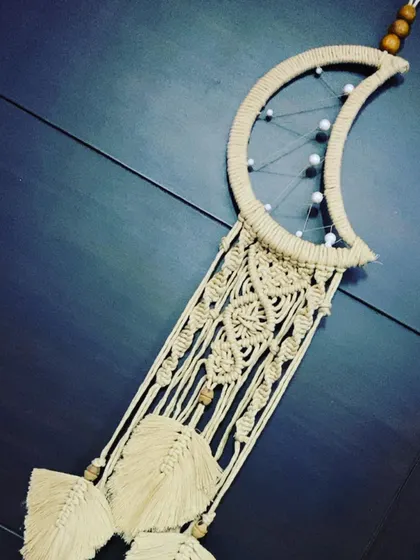 An angled shot of the moon dreamcatcher, showing the intricate knotting and the delicate feathers that hang below.