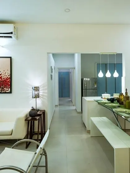 An open-plan apartment living and dining area designed with a clean, white palette. Pops of color are introduced through vibrant artwork and multi-hued cushions, creating a lively and modern atmosphere.