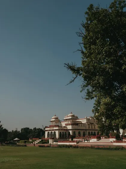 A wide shot of the magnificent Rambagh Palace, showcasing its sprawling lawns and regal presence. This establishes the grand scale of the destination wedding.