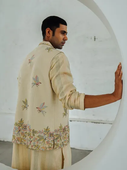 A lookbook image for Wabi Sabi, showcasing a men's bundi jacket with delicate bird embroidery. The circular architectural element frames the model and adds a modern touch.