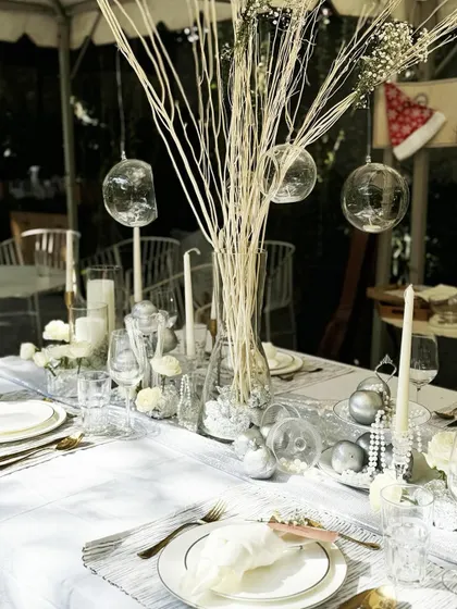 An ethereal tablescape from our workshop, featuring white branches, hanging glass orbs, and a mix of silver-painted pomegranates, pearls, and white roses for a winter wonderland feel.