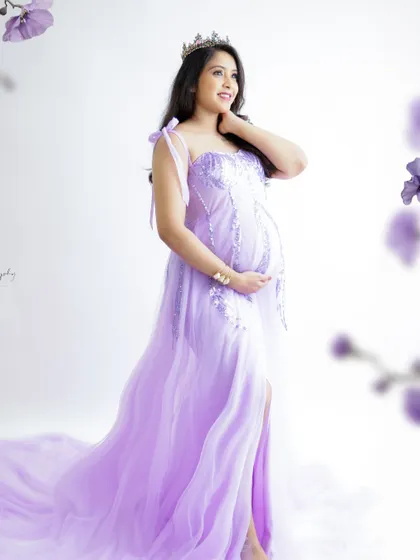 A graceful and elegant portrait. The mom-to-be wears a beautiful lavender gown and a tiara, looking like a princess.