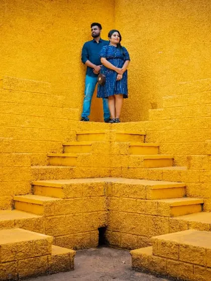 A wide shot of a couple standing atop a unique yellow stepwell, creating a symmetrical and visually powerful pre-wedding photograph.