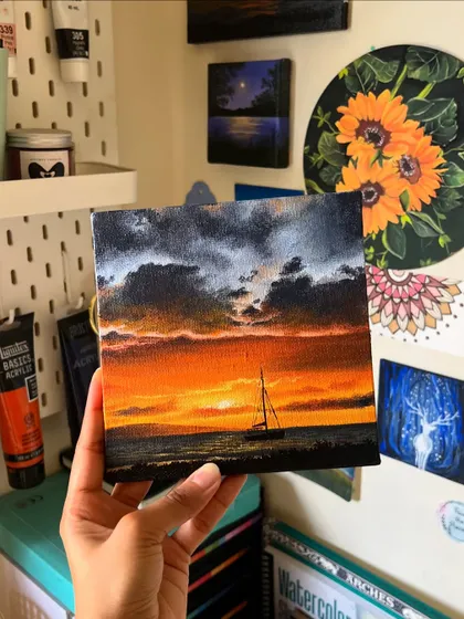 The sailboat sunset painting held up against my studio wall, surrounded by other pieces of my art.