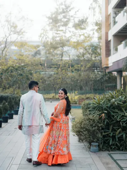 A sweet 'look back at it' moment. The bride glances back with a smile as she leads her groom, a playful and romantic shot from their Haldi day photoshoot.
