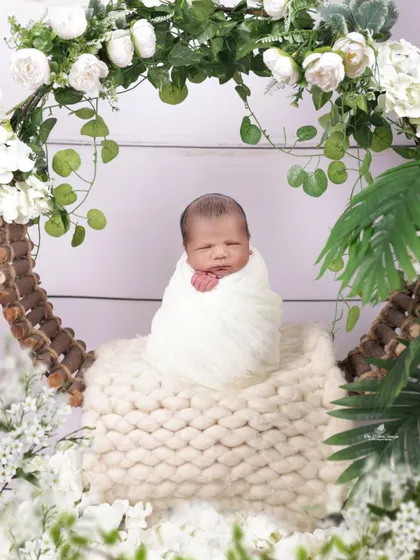 A newborn nestled in a beautiful floral wreath. The contrast between the pure white swaddle and the lush greenery creates a fresh, natural, and artistic portrait.
