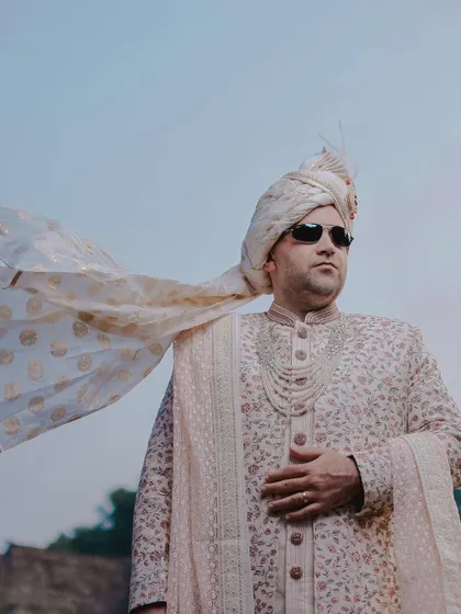 A cool and stylish portrait of the groom in his wedding sherwani and sunglasses. The wind catching his stole adds a dynamic, cinematic flair.