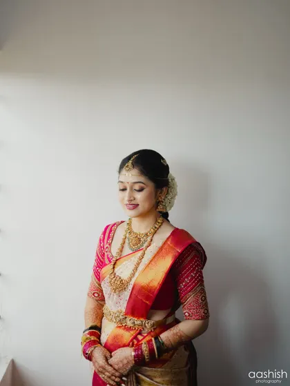 This bride is ready for her big day. Her hair is pulled back in a classic bun adorned with flowers, and her makeup is a perfect example of timeless South Indian bridal beauty.