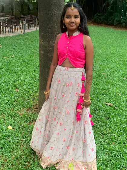 This lovely client is wearing a custom-designed lehenga featuring a bright pink crop top with a mandarin collar. The floral print skirt is finished with playful pink tassels, adding a fun detail to this festive outfit.