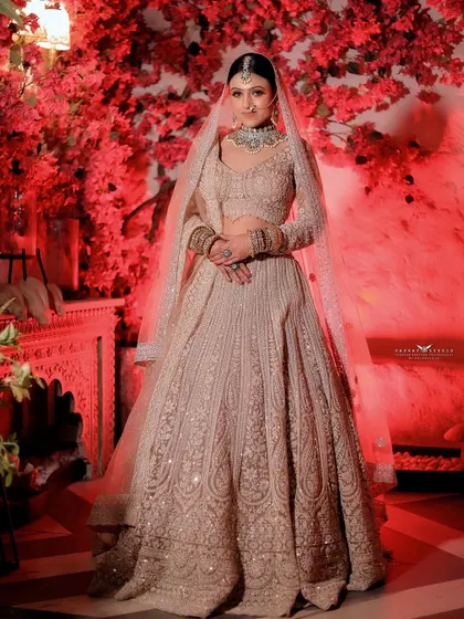 A full-length portrait of the bride against the red floral wall, showcasing the entire elegant ensemble.