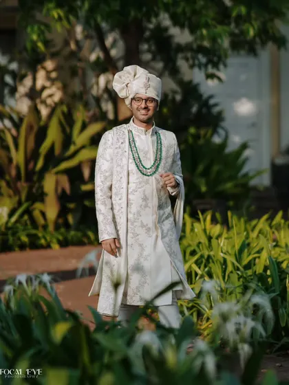 A full-length portrait of the groom looking dapper in his embroidered sherwani and traditional safa, ready for his big day.