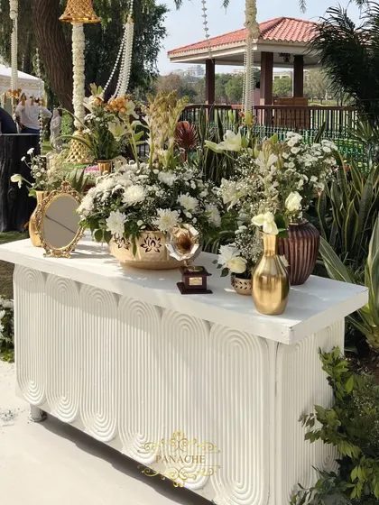 A stylish welcome console table, decorated with an abundance of white flowers, golden vases, and vintage props.