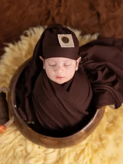 A newborn wrapped snugly in a rich, chocolate-brown swaddle. The baby rests on a soft yellow fur rug, creating a warm and cozy color combination.