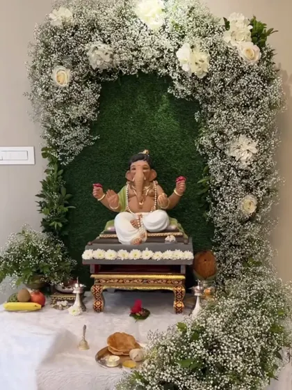 A premium backdrop for a Ganapathi festival. The idol is placed within a beautiful arch of baby's breath and white roses against a green wall, creating a fresh and elegant look.