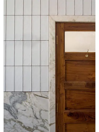 A detail shot from Apartment 5026, showing the junction of a reclaimed teak door, marble trim, and simple white tiles. It is in these moments of material intersection that the character of a home is truly defined.