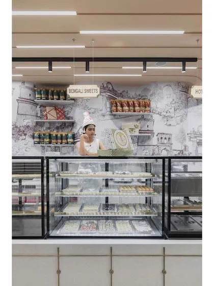 A view of the sweets counter, set against a custom wallpaper depicting the historic Gummanayaka fort. This artwork by Trupty Somaiah enriches the space with a strong sense of place and history.
