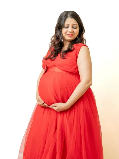 A beautiful solo portrait of the mom-to-be in a vibrant red gown. The focus is on her serene expression as she looks down at her bump, a classic and timeless maternity pose.