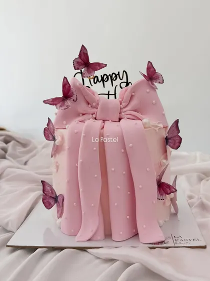 A pretty pink cake featuring a large, beautifully crafted pink bow and delicate butterflies. It's a very trendy and feminine design, perfect for a stylish birthday.