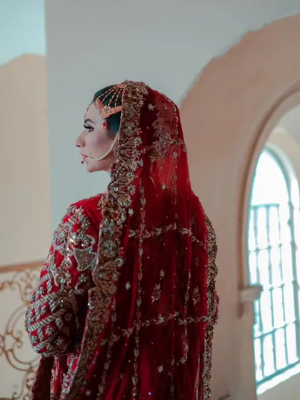 A side-profile portrait of the bride, highlighting the intricate details of her dupatta and the elegant line of her nose ring.