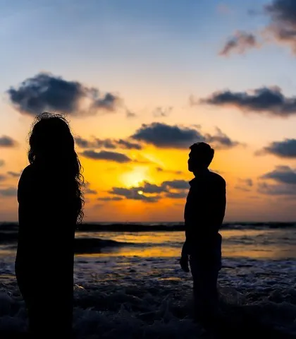 A silhouette of the couple standing apart, facing each other against a dramatic sunset. The space between them creates a sense of anticipation and connection.