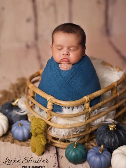 A 38-day-old baby boy wrapped in a deep blue swaddle, nestled in a basket with rustic pumpkins. This autumn-inspired theme is perfect for babies born in the fall.