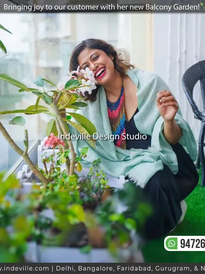 The joy of a green transformation. Here's a happy client enjoying her new balcony garden, complete with custom white planters, artificial grass flooring, and a comfortable seating area, all with a stunning city view.