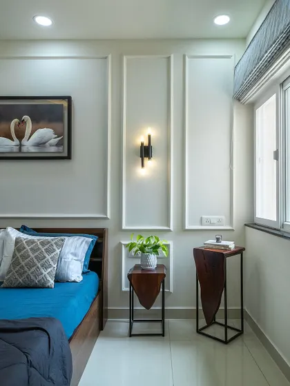 Wall moldings and classic sconce lighting add a touch of timeless elegance to the master bedroom, complementing the modern furniture.