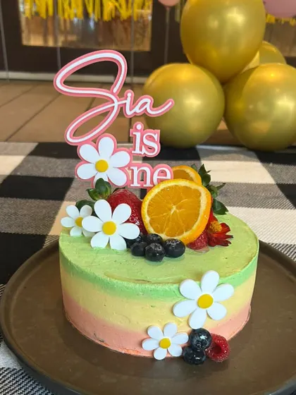 "Sia is One." This sweet and simple layered acrylic topper looks beautiful on a fruit-topped cake. The daisies add a fresh, summery feel.