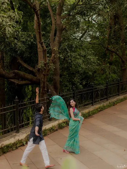 A playful, Bollywood-style moment in a park, with the groom catching the bride's saree pallu.