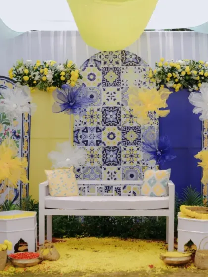 A Haldi setup with a unique backdrop of blue and yellow patterned tiles, creating a fresh and modern look while keeping the traditional yellow theme.