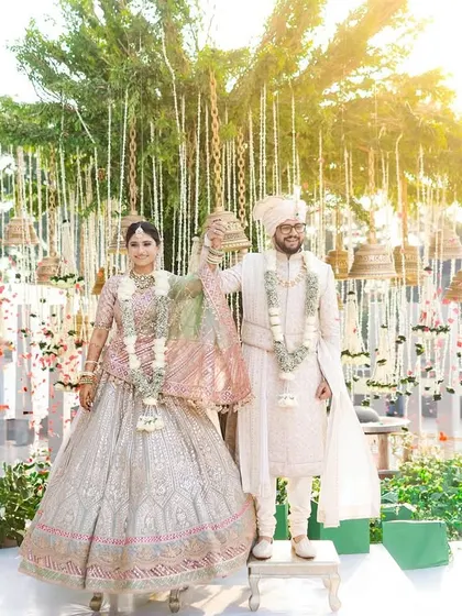 A beautiful, sun-kissed portrait of the couple after their Varmala ceremony, standing together under a canopy of hanging bells.