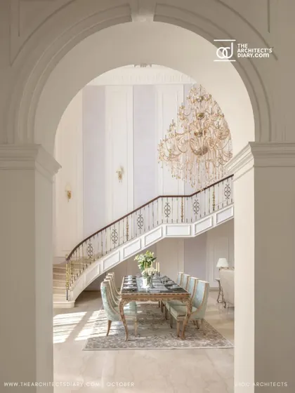 A view of the grand dining area through a classical archway in The Ivory Royale. This framing creates a sense of discovery and highlights the majestic staircase and chandelier in the background.