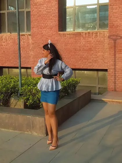 This pose shows off the full silhouette of the peplum top and mini skirt combination. The headband adds a preppy, playful touch to the outfit.