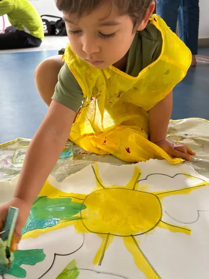 A child experiments with mixing yellow and green paint, discovering color theory in the most hands-on way possible.