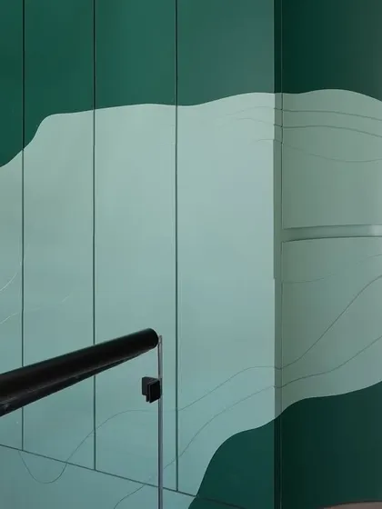 A close-up of the custom green paneling in the staircase well. The layered, topographic-like design conceals a secondary access door, seamlessly blending functionality with artistic expression.