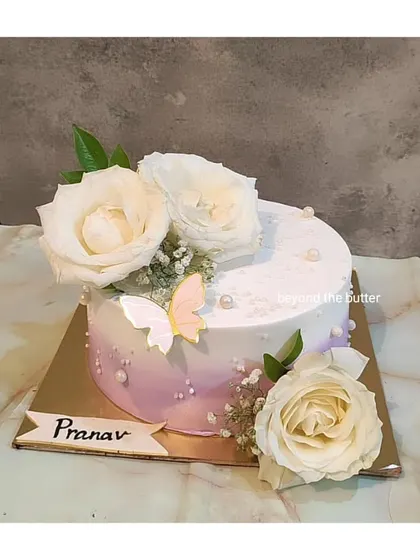 An elegant white cake with a hint of lavender ombre. It's decorated with beautiful white roses and a single butterfly for a touch of whimsy.