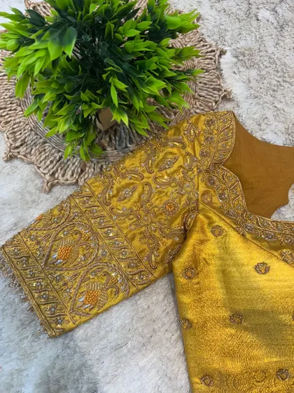 A mustard yellow blouse with heavy, all-over gold embroidery, showcasing intricate patterns on the sleeves.