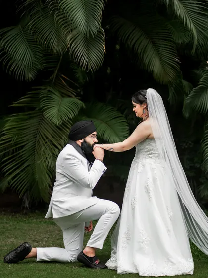 A chivalrous moment as the groom kisses his bride's hand in a lush garden setting.