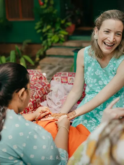 A guest laughs with delight as she gets her Mehendi applied, enjoying the festive and social aspect of the ritual.