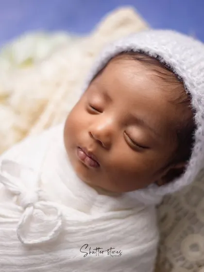 A close-up portrait of a baby in a white bonnet, focusing on their peaceful sleeping face.