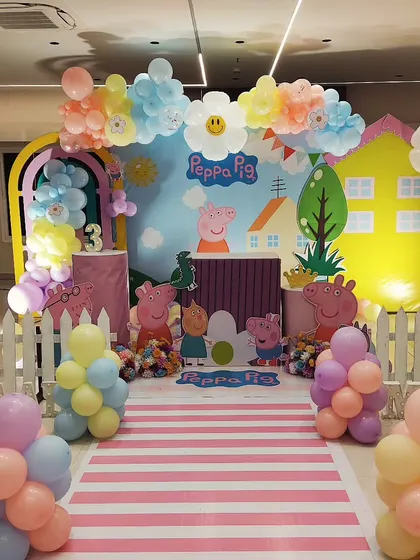 A cheerful Peppa Pig theme for a third birthday. I recreated Peppa's world with a house backdrop, character cutouts, a picket fence, and a striped walkway, all framed by colorful balloon clouds.