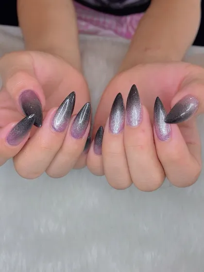 A dramatic ombré glitter effect on sharp stiletto nails. The color fades from a soft pink at the base to a deep, glittery black at the tips for a truly magical look.