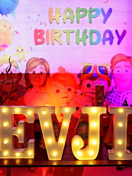 The birthday boy's name, Devjit, in light-up marquee letters, set against a Cocomelon backdrop. This is a popular add-on that personalizes the decor and looks great in photos.