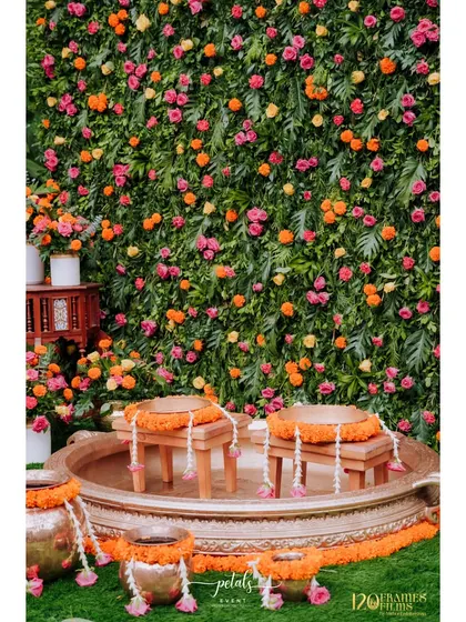 A close-up of the Haldi seating area, with small wooden stools placed inside a large urli. The surrounding flower wall adds a touch of natural beauty and color.