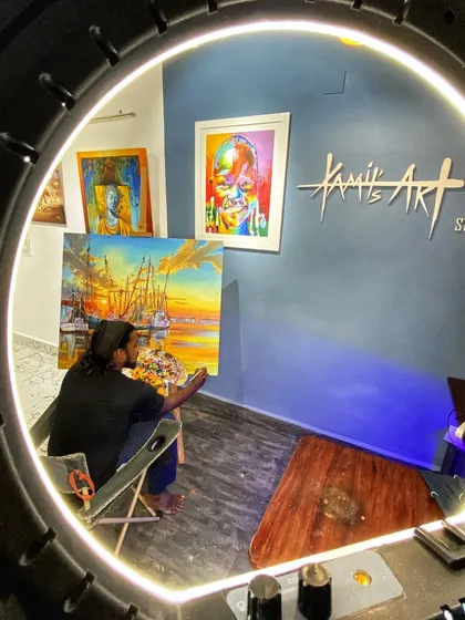 A creative shot of my studio seen through my ring light, where I am working on a large painting of a ship at sunset.