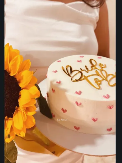 A simple and sweet 'Bride to Be' cake, held next to a bright sunflower. The hand-painted hearts add a personal and charming touch.