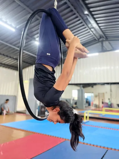 Finding focus and calm while inverted. This student holds a tucked pose on the aerial hoop, a great exercise for building core stability and body control.