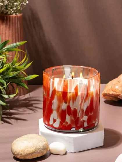 A lifestyle shot of a red and white marbled glass candle from Lighthouse. The warm, earthy tones of the background create a cozy and inviting atmosphere.