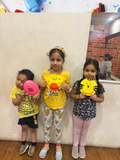 Three friends proudly display their finished paper plate animals. Our art classes are a great social activity where kids can create alongside their peers.